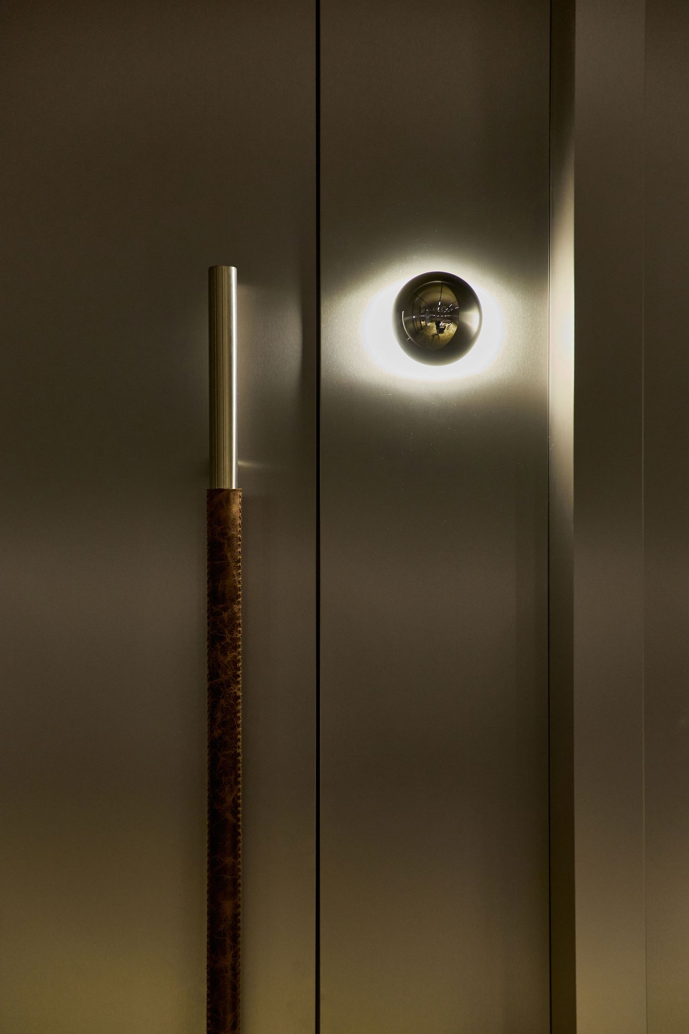 A sleek, modern door with a metallic handle and circular light fixture, casting a soft halo glow on a textured surface.