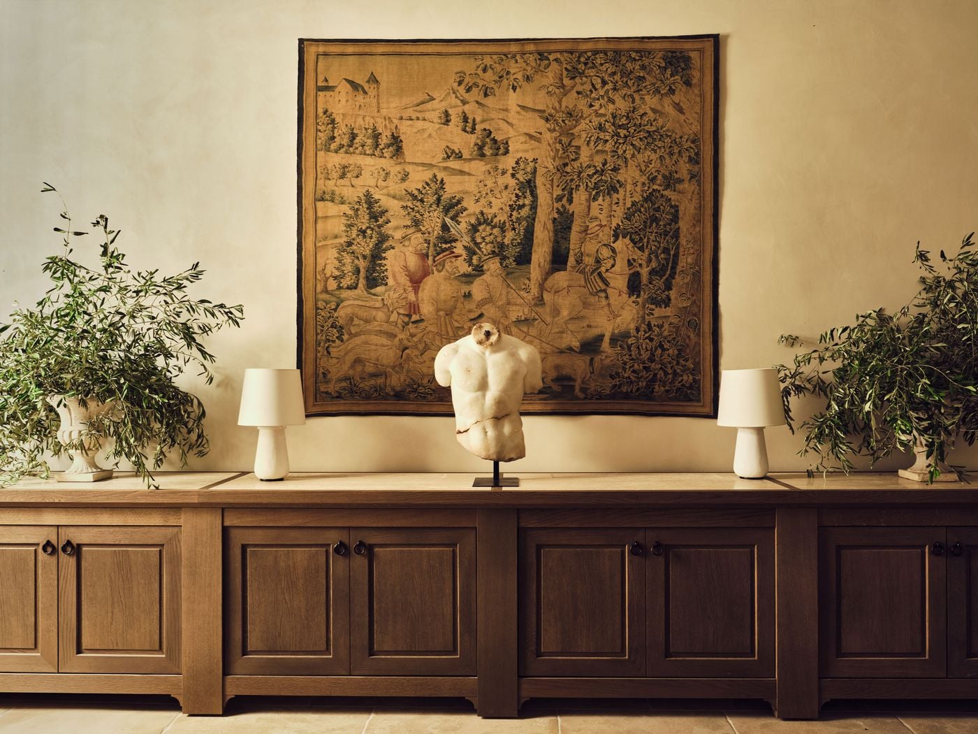 An antique tapestry of a hunting party, with hounds, horsemen and a hilltop castle, hangs above a long oak sideboard at La Réserve Firenze. A fractured white marble torso on a slim stand sits at its centre, flanked by sculptural lamps and stone urns overflowing with olive branches. An antique tapestry of a hunting party, with hounds, horsemen and a hilltop castle, hangs above a long oak sideboard at La Réserve Firenze. A fractured white marble torso on a slim stand sits at its centre, flanked by sculptural lamps and stone urns overflowing with olive branches.