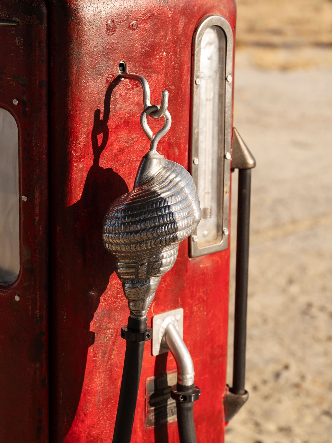 Close-up of a vintage red gas pump with a metallic nozzle and hose, featuring a hook and a distinct textured design.