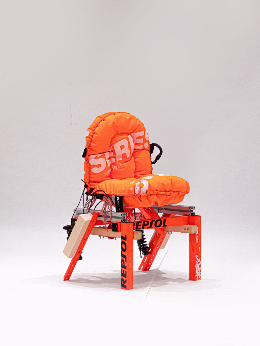 A bright orange, padded chair with visible branding, supported by a sleek, red frame, featuring electronic wiring and a modern design. A bright orange, padded chair with visible branding, supported by a sleek, red frame, featuring electronic wiring and a modern design.