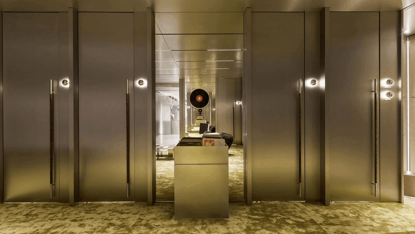 A modern hallway with sleek metallic doors, warm lighting, and plush green carpet, featuring a vintage record player in the background. A modern hallway with sleek metallic doors, warm lighting, and plush green carpet, featuring a vintage record player in the background.