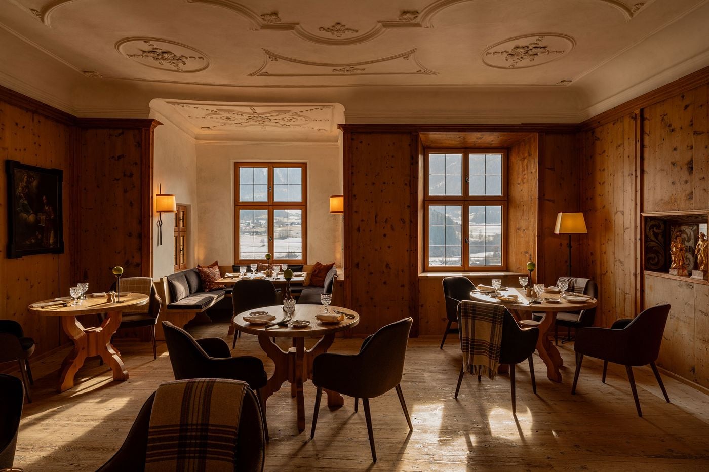 Winter sunlight slants across worn floorboards in a Castel Badia dining room crowned by delicate stucco medallions. A corner banquette with patterned cushions nestles beneath a mullioned window, while an old devotional painting, gilded saints in a painted niche and checked wool throws lend layered warmth. Winter sunlight slants across worn floorboards in a Castel Badia dining room crowned by delicate stucco medallions. A corner banquette with patterned cushions nestles beneath a mullioned window, while an old devotional painting, gilded saints in a painted niche and checked wool throws lend layered warmth.