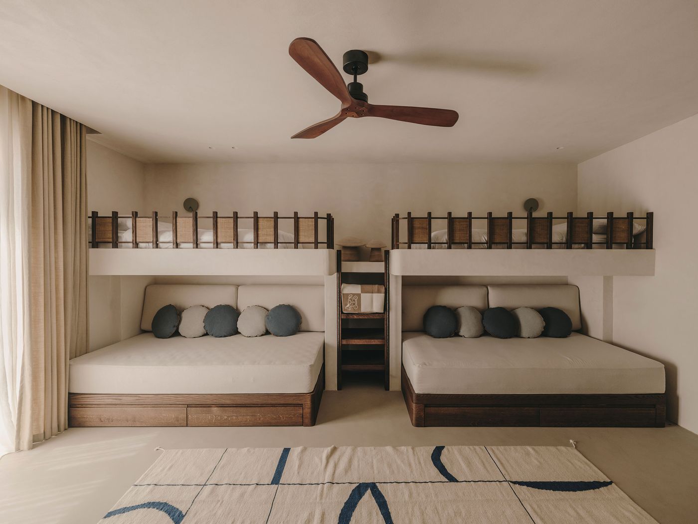 A stylish bedroom featuring two cozy bunk beds above two built-in sofas, soft cushions, a ceiling fan, and natural light streaming through curtains. A stylish bedroom featuring two cozy bunk beds above two built-in sofas, soft cushions, a ceiling fan, and natural light streaming through curtains.