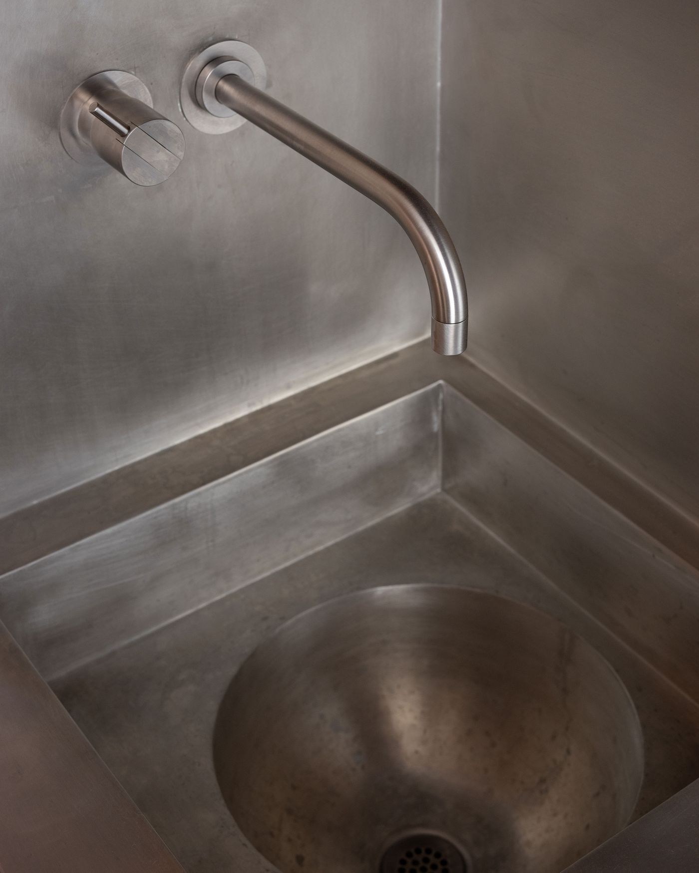 Close-up of a modern stainless steel sink with a sleek faucet and control handle, showcasing a minimalist design.