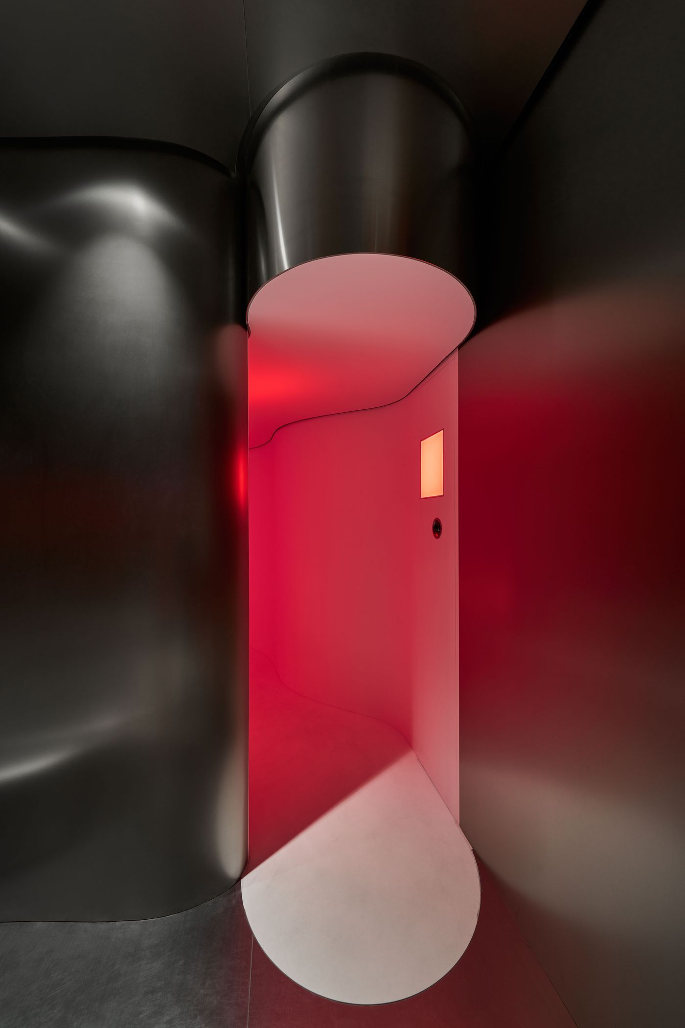A modern, curved hallway with sleek black walls, illuminated by a soft red glow, features a circular white floor design and a small screen. A modern, curved hallway with sleek black walls, illuminated by a soft red glow, features a circular white floor design and a small screen.