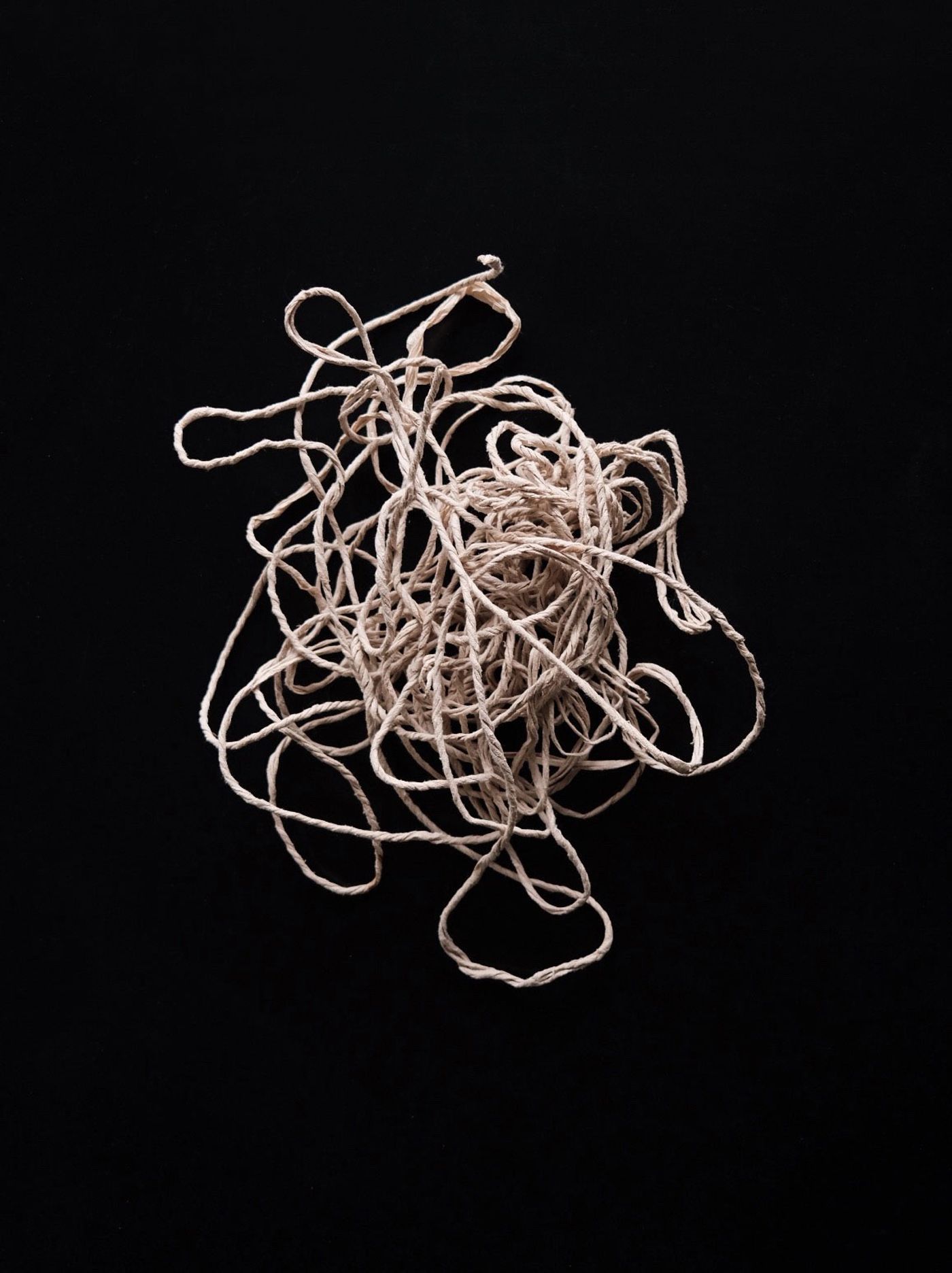 A tangled mass of light-colored string on a black background, showcasing its intricate loops and knots. A tangled mass of light-colored string on a black background, showcasing its intricate loops and knots.