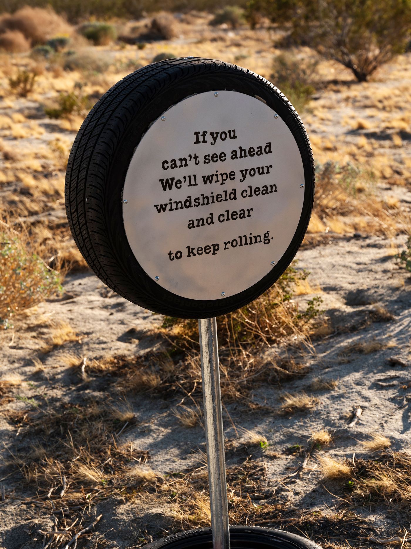 A roadside sign shaped like a tire, featuring a motivational message about keeping clear to drive forward. Surrounding desert landscape is visible.
