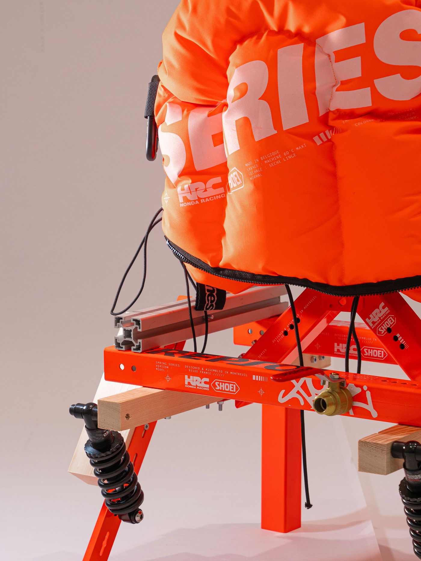 A close-up of a vibrant orange racing seat with large "SERIES" text, mounted on a sturdy frame with a shock absorber. A close-up of a vibrant orange racing seat with large "SERIES" text, mounted on a sturdy frame with a shock absorber.