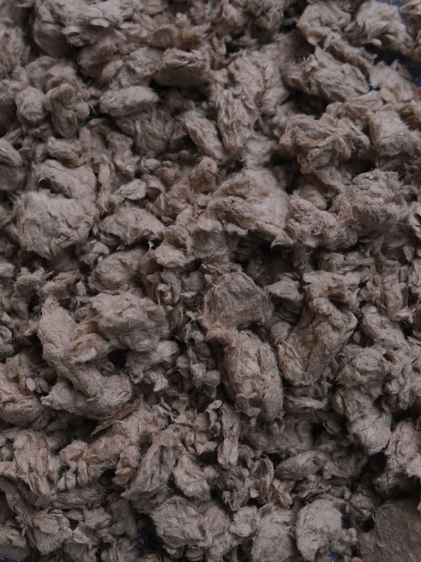 A close-up view of coarse, brown plant fibers resembling shredded paper or insulation material, densely packed together. A close-up view of coarse, brown plant fibers resembling shredded paper or insulation material, densely packed together.