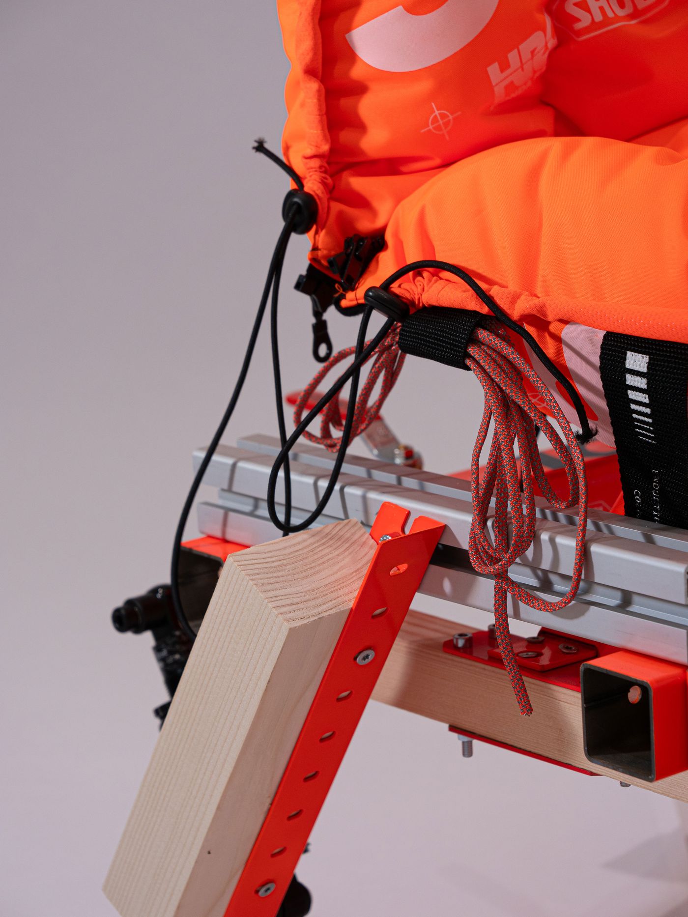 Close-up of an orange padded seat harness, with ropes and wood fixtures attached to a metal frame, highlighting its sturdy construction. Close-up of an orange padded seat harness, with ropes and wood fixtures attached to a metal frame, highlighting its sturdy construction.