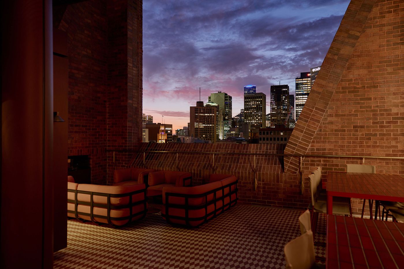 A rooftop terrace with modern furniture overlooks a vibrant city skyline at sunset, with dramatic clouds and twinkling lights. A rooftop terrace with modern furniture overlooks a vibrant city skyline at sunset, with dramatic clouds and twinkling lights.