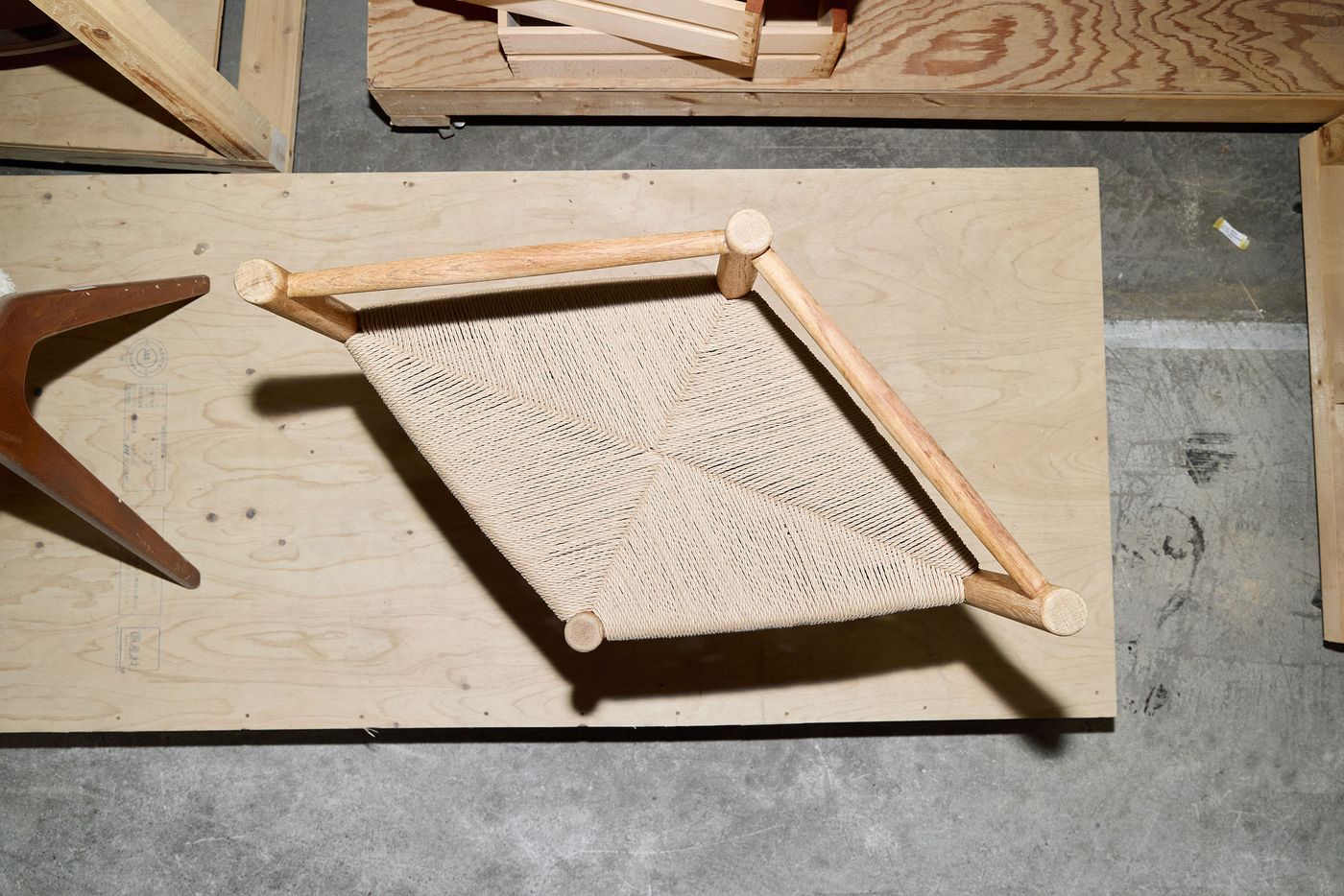 Top view of a woven seat chair with wooden frame, placed on a wooden surface in a workshop setting.