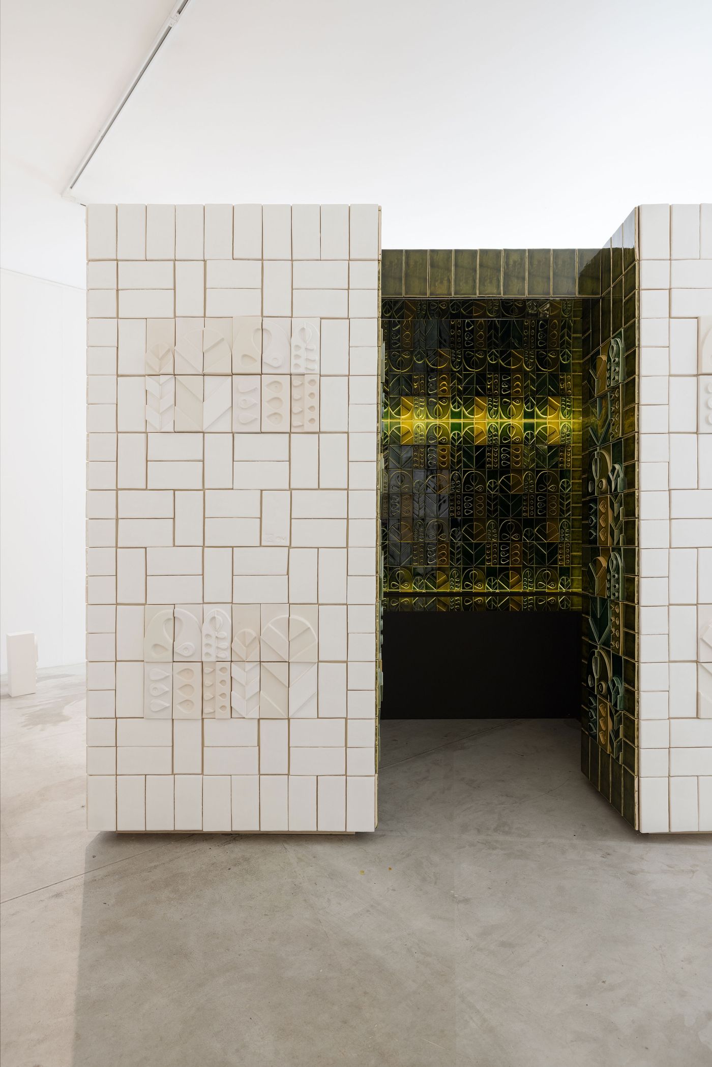 An architectural installation from the "Arcadia" exhibition by Oficina Marques, Viúva Lamego and Spacegram Studio features an immersive space crafted from white and glazed green ceramic tiles. The exterior showcases textured white tiles with subtle relief patterns, while the interior glows with vibrant green and yellow glazed tiles, creating a rich interplay of light and artisanal texture. An architectural installation from the "Arcadia" exhibition by Oficina Marques, Viúva Lamego and Spacegram Studio features an immersive space crafted from white and glazed green ceramic tiles. The exterior showcases textured white tiles with subtle relief patterns, while the interior glows with vibrant green and yellow glazed tiles, creating a rich interplay of light and artisanal texture.