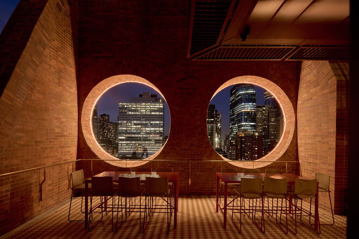 A cozy dining area with a modern table and chairs, framed by large, illuminated circular windows showcasing a city skyline at dusk. A cozy dining area with a modern table and chairs, framed by large, illuminated circular windows showcasing a city skyline at dusk.