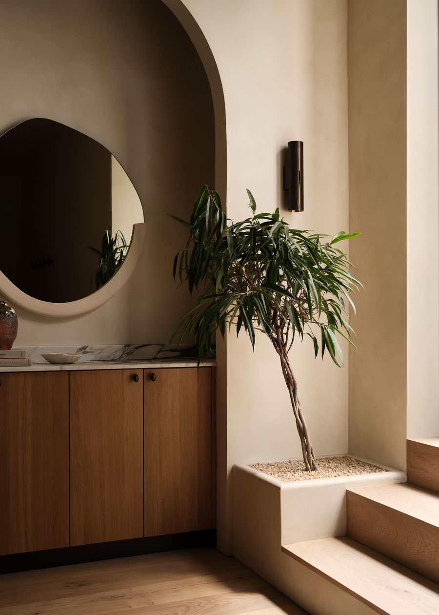 A serene interior with wooden cabinetry, a round mirror, and a potted tree beside a stone-lined planter, softly lit by wall sconces. A serene interior with wooden cabinetry, a round mirror, and a potted tree beside a stone-lined planter, softly lit by wall sconces.