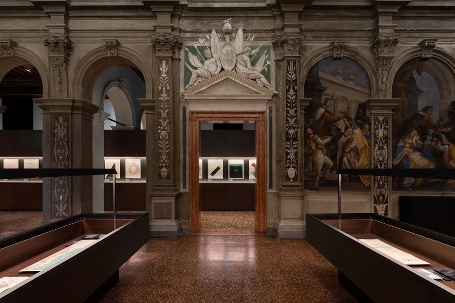A gallery interior featuring ornate architecture, framed artworks, and display cases, creating a sophisticated atmosphere.