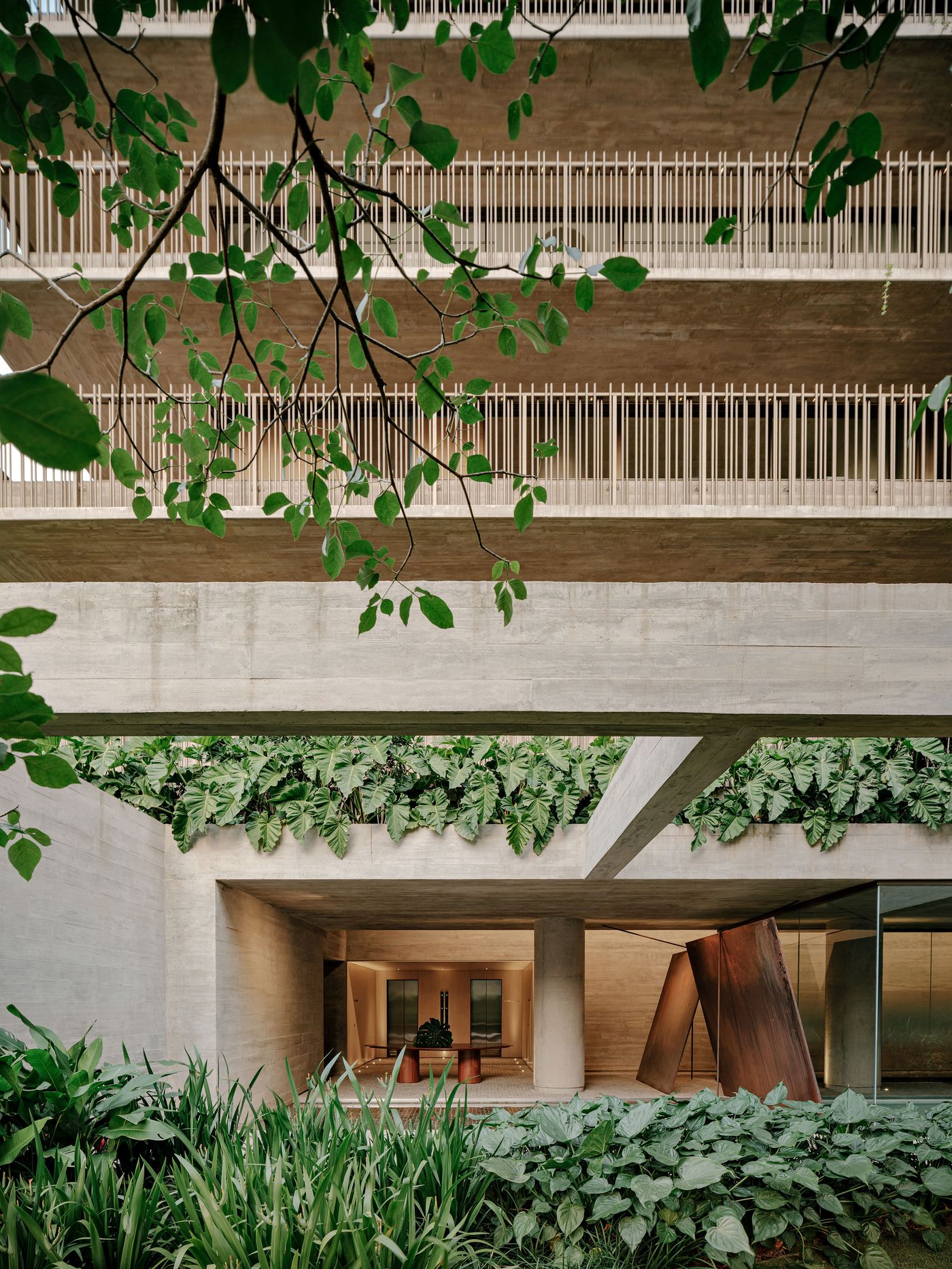 The lower levels of this striking brutalist architecture, where massive concrete beams are softened by lush, cascading philodendron plants. The interplay of raw concrete, verdant foliage, and glimpses into the warm, illuminated interiors creates a compelling dialogue between nature and structured design, reflecting a biophilic approach. The lower levels of this striking brutalist architecture, where massive concrete beams are softened by lush, cascading philodendron plants. The interplay of raw concrete, verdant foliage, and glimpses into the warm, illuminated interiors creates a compelling dialogue between nature and structured design, reflecting a biophilic approach.