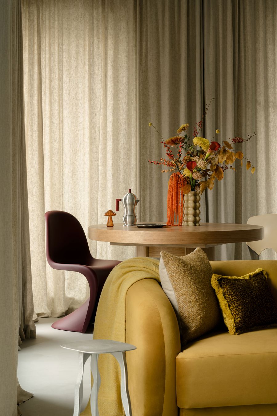 A close-up of the dining area reveals a sculptural burgundy Panton chair and playful ceramic vases in rich tones. Set against floor-to-ceiling drapes and a soft-toned interior, the scene captures the interplay of midcentury modern curves with curated eclecticism. A close-up of the dining area reveals a sculptural burgundy Panton chair and playful ceramic vases in rich tones. Set against floor-to-ceiling drapes and a soft-toned interior, the scene captures the interplay of midcentury modern curves with curated eclecticism.