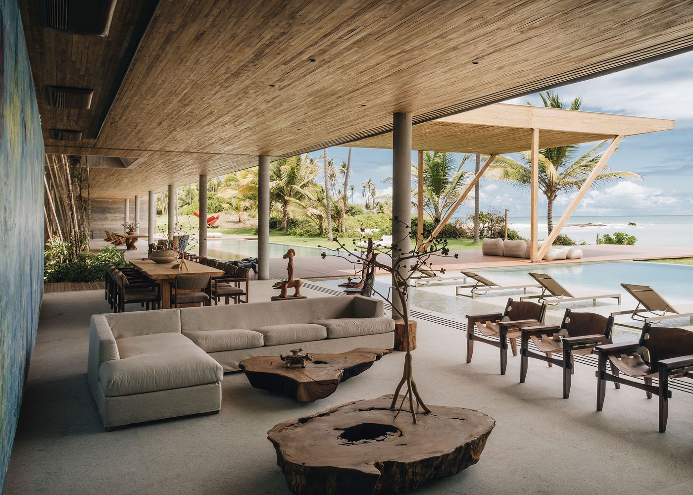 An elegant open-concept living area featuring a comfortable sofa, wooden dining table, and views of a pool and palm trees outside.