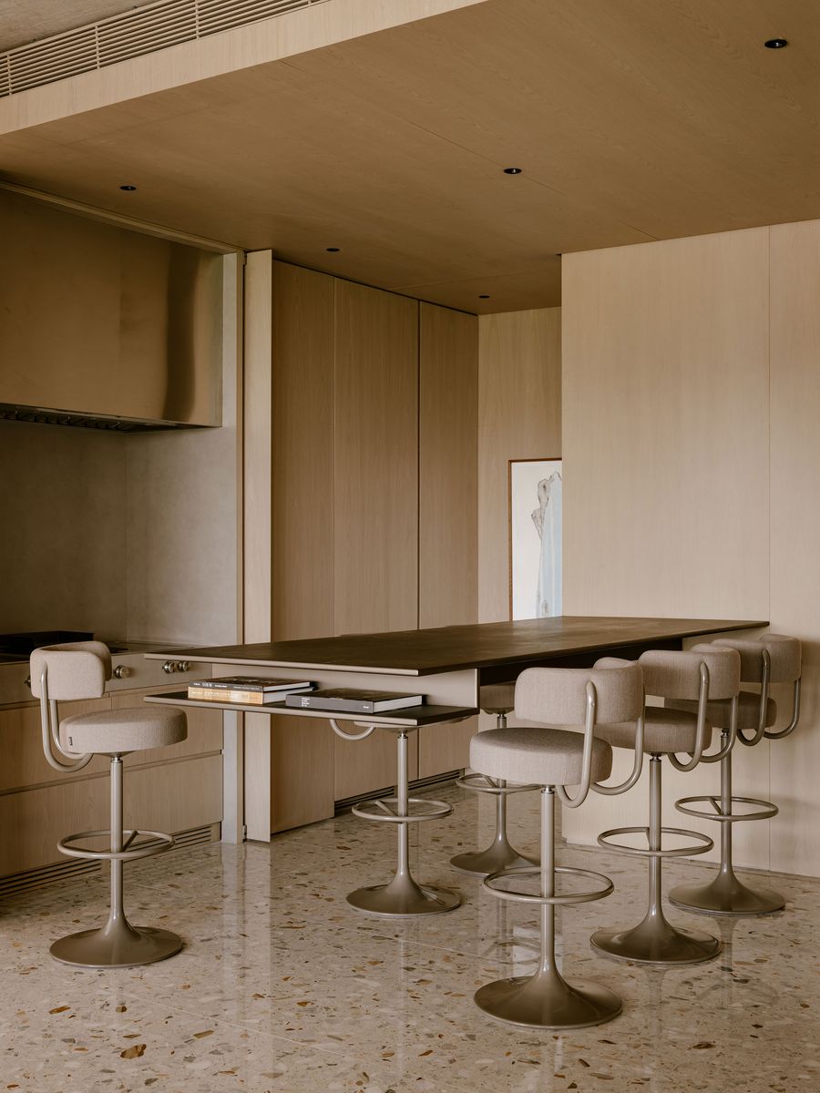 A minimalist kitchen featuring a wooden bar table with textured surface and stylish beige stools, complemented by light wooden cabinetry. A minimalist kitchen featuring a wooden bar table with textured surface and stylish beige stools, complemented by light wooden cabinetry.