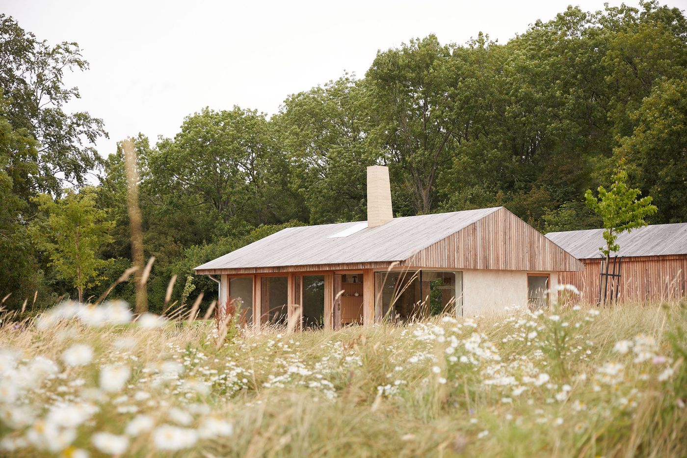 The Maker's Barn, designed by Hutch Design, presents a contemporary take on rustic architecture, nestled amidst tall golden grasses and wildflowers. Its light timber-clad exterior, punctuated by floor-to-ceiling windows and a prominent pale chimney, integrates subtly with the dense green foliage behind, exuding a quiet, secluded atmosphere. The Maker's Barn, designed by Hutch Design, presents a contemporary take on rustic architecture, nestled amidst tall golden grasses and wildflowers. Its light timber-clad exterior, punctuated by floor-to-ceiling windows and a prominent pale chimney, integrates subtly with the dense green foliage behind, exuding a quiet, secluded atmosphere.