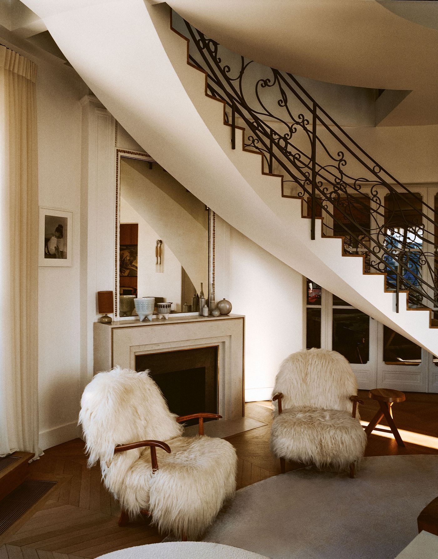 A grand staircase with an ornate wrought-iron balustrade elegantly sweeps upwards, dominating the composition. Below, two plush, shaggy armchairs offer a luxurious tactile contrast to the smooth, minimalist fireplace, creating a harmonious blend of classic Parisian grandeur and contemporary comfort. A grand staircase with an ornate wrought-iron balustrade elegantly sweeps upwards, dominating the composition. Below, two plush, shaggy armchairs offer a luxurious tactile contrast to the smooth, minimalist fireplace, creating a harmonious blend of classic Parisian grandeur and contemporary comfort.