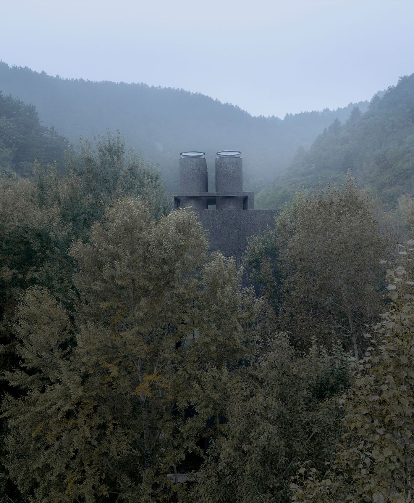 A misty landscape featuring a dark, modern building with two cylindrical chimneys, surrounded by trees and rolling hills. A misty landscape featuring a dark, modern building with two cylindrical chimneys, surrounded by trees and rolling hills.