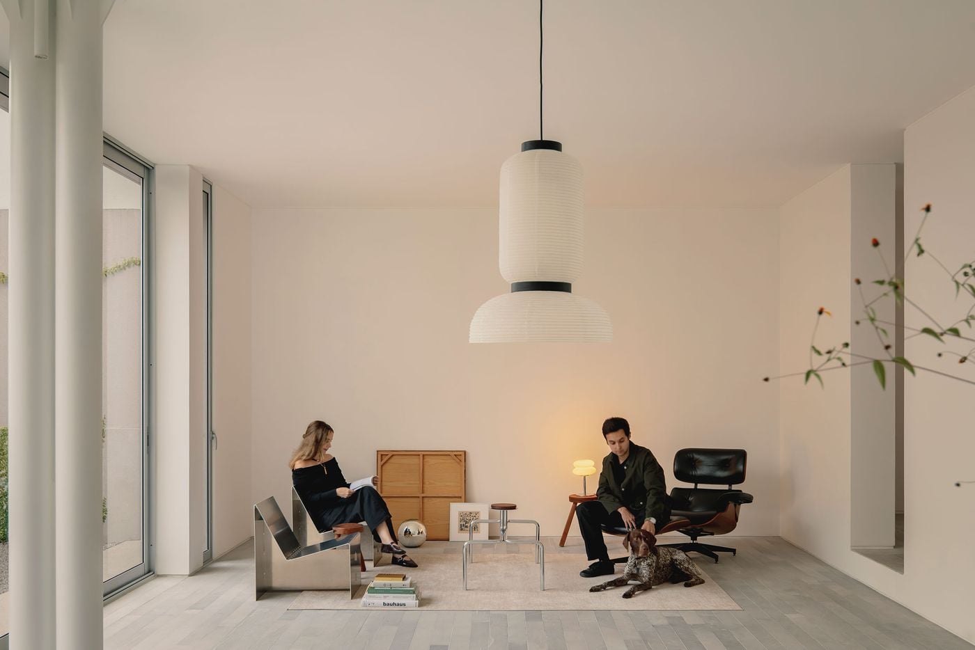 Casa Tlaloc’s minimalist living room pairs white walls and pale grey stone flooring with a carefully edited mix of sculptural metal seating, warm timber accents and black leather. A large paper pendant anchors the otherwise spare composition as two occupants and their dog bring an informal domestic presence to the space. Casa Tlaloc’s minimalist living room pairs white walls and pale grey stone flooring with a carefully edited mix of sculptural metal seating, warm timber accents and black leather. A large paper pendant anchors the otherwise spare composition as two occupants and their dog bring an informal domestic presence to the space.