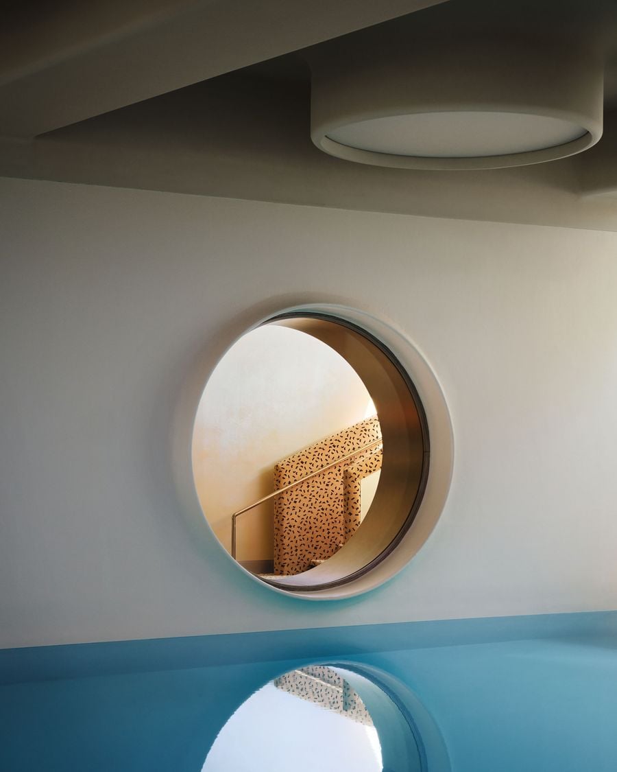 A circular window links the Ken Club’s turquoise indoor pool to the adjoining circulation space, framing a view of the flecked staircase beyond. Soft grey surfaces and oversized round ceiling lights give the pool area a calm, retro-futurist character, with water reflections amplifying the geometry. A circular window links the Ken Club’s turquoise indoor pool to the adjoining circulation space, framing a view of the flecked staircase beyond. Soft grey surfaces and oversized round ceiling lights give the pool area a calm, retro-futurist character, with water reflections amplifying the geometry.