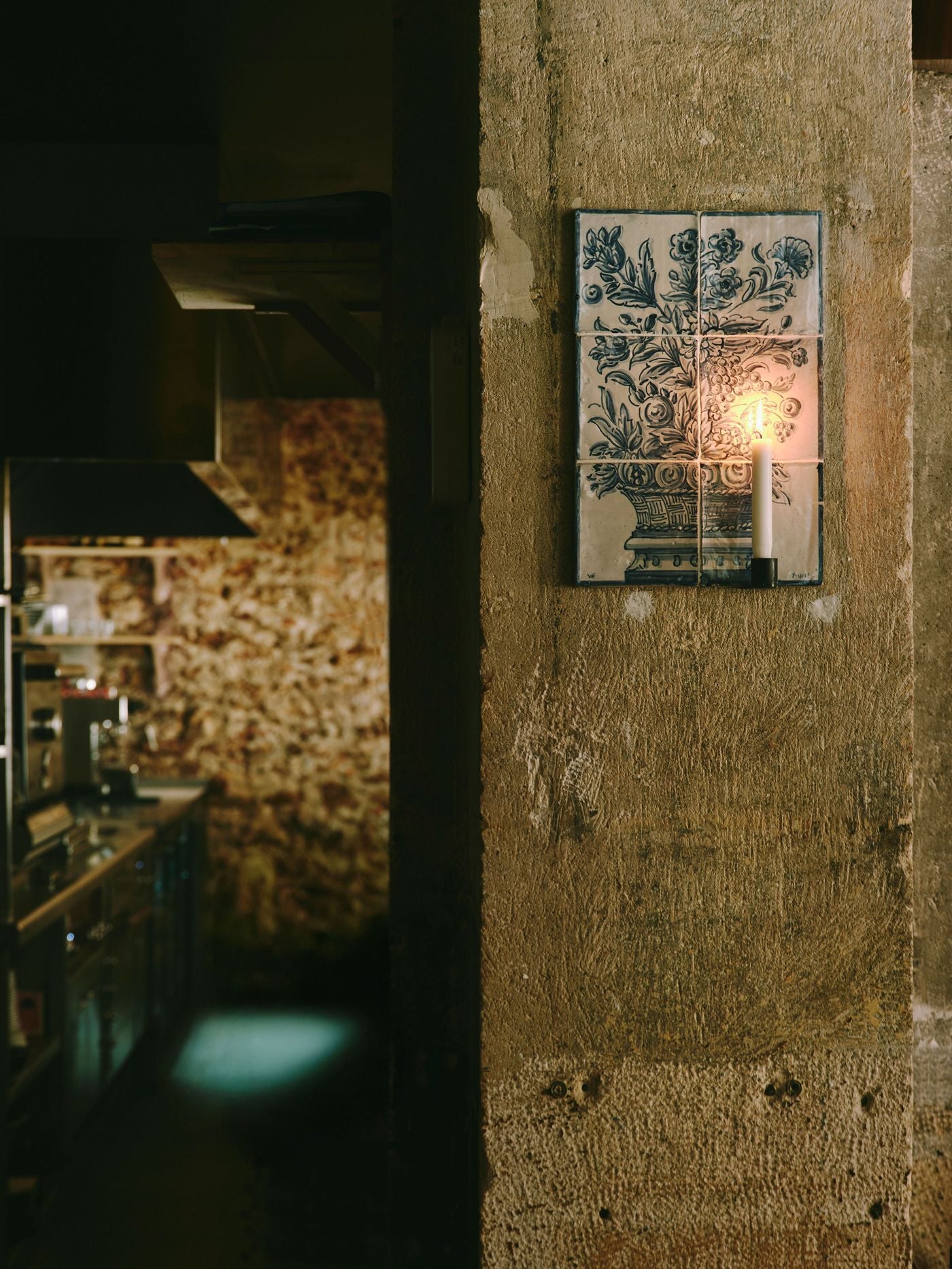 A hand-painted azulejo panel of a flower-filled urn hangs on a pitted concrete pillar at SaltoBar in Paris. A single candle is mounted directly onto its surface, and the flame warms the cobalt blooms. In the shadowy background, the kitchen's stainless-steel fittings and mottled stone wall recede into soft focus. A hand-painted azulejo panel of a flower-filled urn hangs on a pitted concrete pillar at SaltoBar in Paris. A single candle is mounted directly onto its surface, and the flame warms the cobalt blooms. In the shadowy background, the kitchen's stainless-steel fittings and mottled stone wall recede into soft focus.