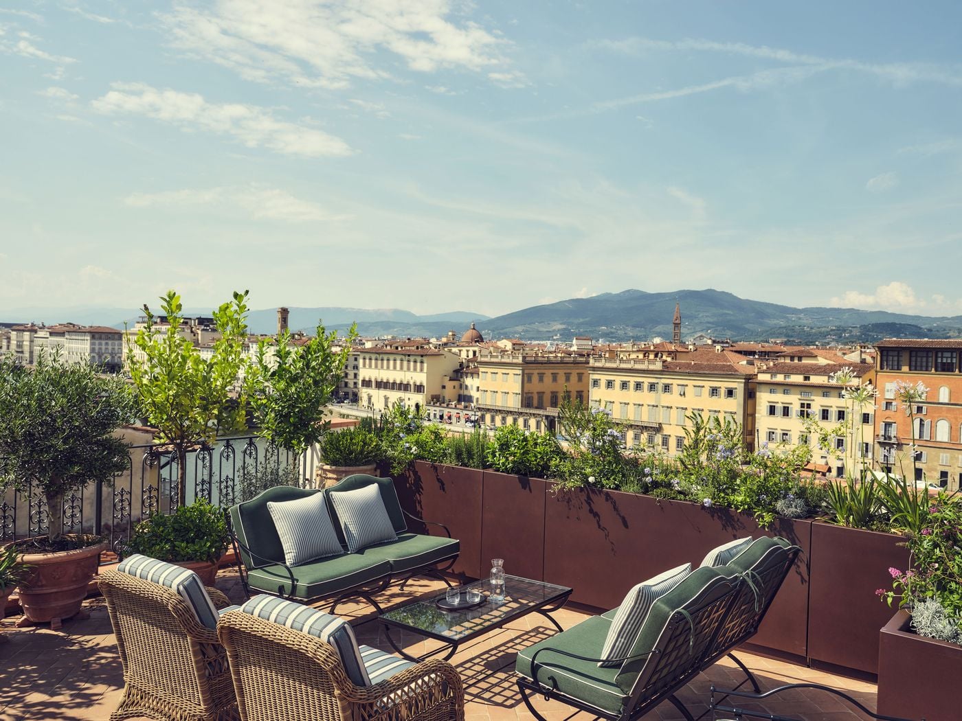 The rooftop terrace at La Réserve Firenze looks out across the Arno to a sweep of ochre palazzi, domes and bell towers, with hills rising beyond. Green-cushioned iron sofas, wicker armchairs in striped upholstery and weathered steel planters of plumbago, rosemary and citrus trees frame the panorama. The rooftop terrace at La Réserve Firenze looks out across the Arno to a sweep of ochre palazzi, domes and bell towers, with hills rising beyond. Green-cushioned iron sofas, wicker armchairs in striped upholstery and weathered steel planters of plumbago, rosemary and citrus trees frame the panorama.