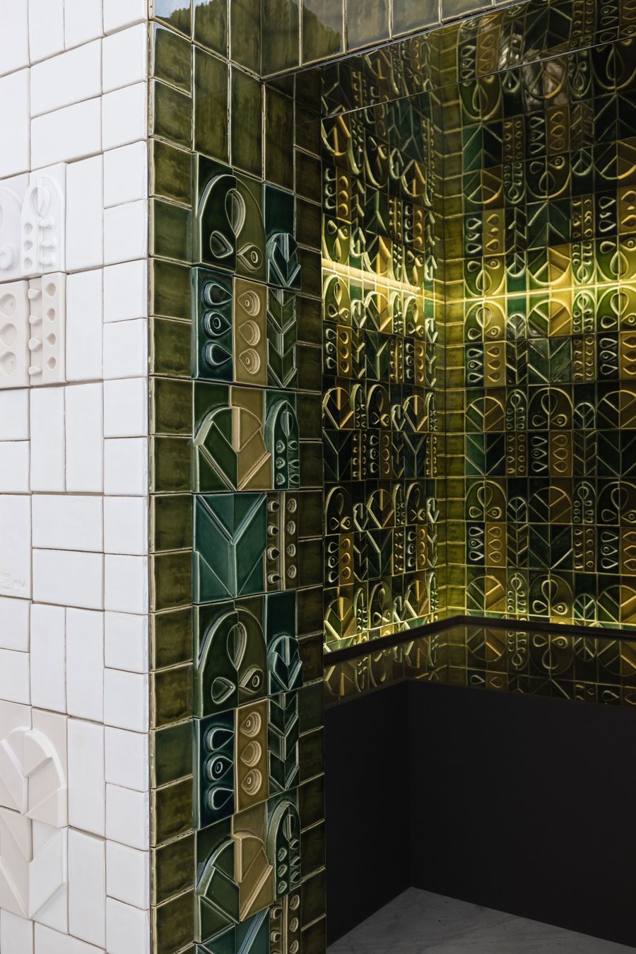 A captivating detail from the "Arcadia" exhibition by Oficina Marques, Viúva Lamego and Spacegram Studio, showcasing an corner installation crafted from rich, variegated green and golden glazed ceramic tiles. The tiles feature intricate geometric and organic relief patterns, reflecting light beautifully and creating a luxurious, textural interplay of traditional craftsmanship and modern design. A captivating detail from the "Arcadia" exhibition by Oficina Marques, Viúva Lamego and Spacegram Studio, showcasing an corner installation crafted from rich, variegated green and golden glazed ceramic tiles. The tiles feature intricate geometric and organic relief patterns, reflecting light beautifully and creating a luxurious, textural interplay of traditional craftsmanship and modern design.