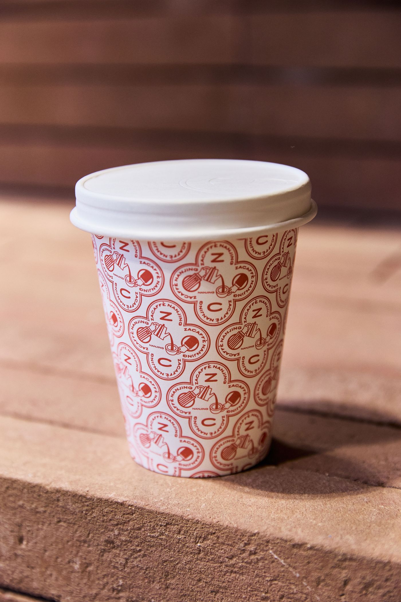A coffee cup with a whimsical red pattern sits on a wooden surface, featuring playful illustrations of coffee-related themes. A coffee cup with a whimsical red pattern sits on a wooden surface, featuring playful illustrations of coffee-related themes.