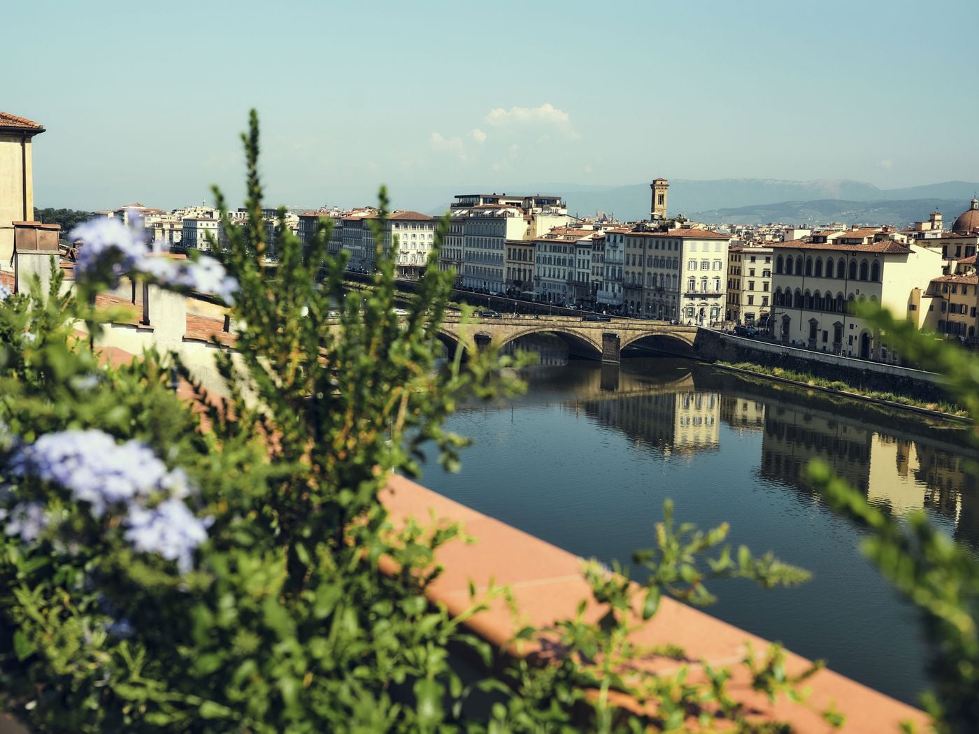 Framed by soft-focus plumbago on the terrace of La Réserve Firenze, the Arno curves beneath an arched stone bridge, its still surface mirroring the pale facades of the opposite bank. Terracotta rooftops, a distant bell tower and blue hills complete a quintessentially Florentine view. Framed by soft-focus plumbago on the terrace of La Réserve Firenze, the Arno curves beneath an arched stone bridge, its still surface mirroring the pale facades of the opposite bank. Terracotta rooftops, a distant bell tower and blue hills complete a quintessentially Florentine view.