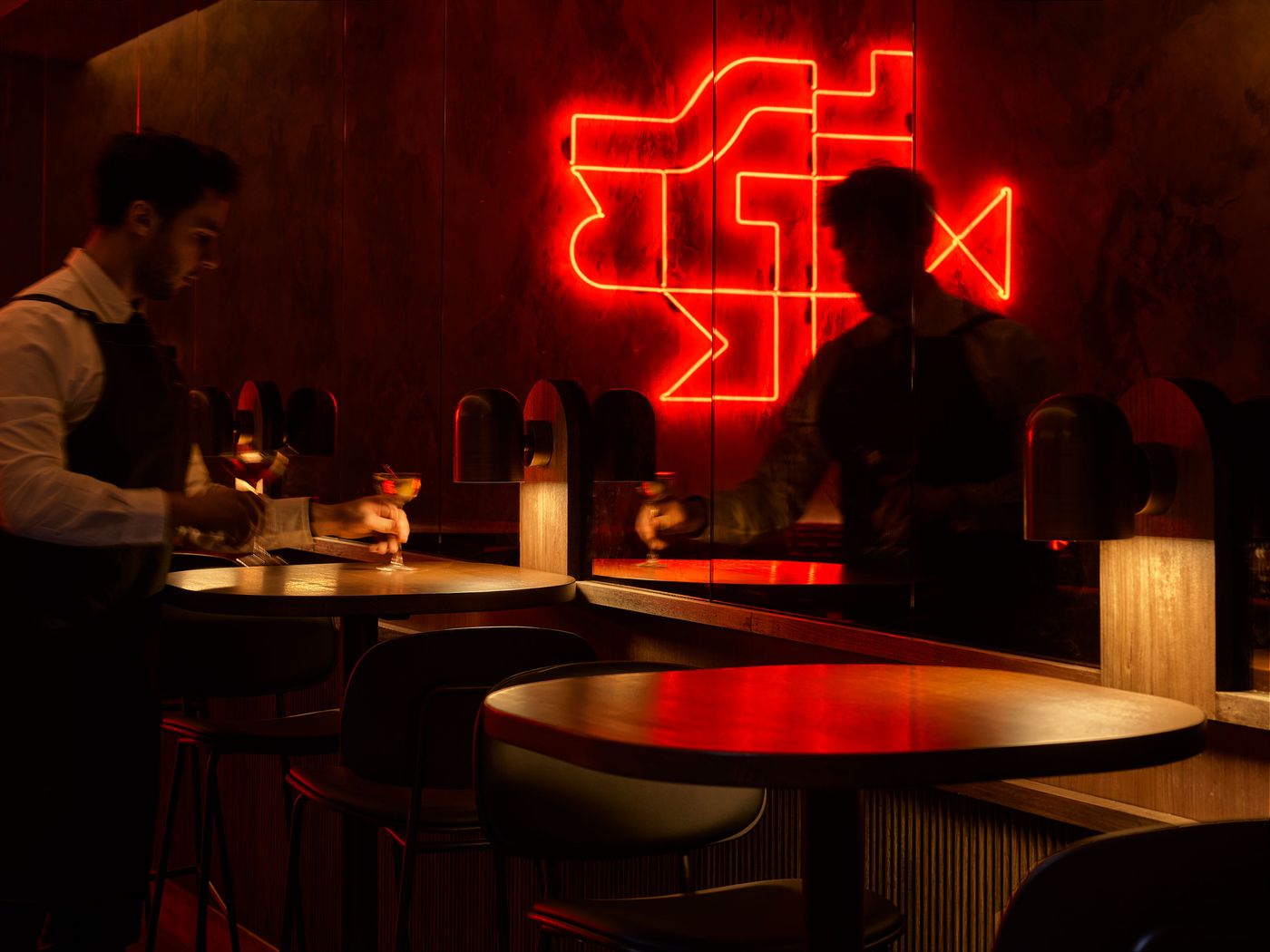 A dimly lit bar with sleek decor, featuring a glowing red neon sign, where a bartender prepares cocktails at a wooden counter. A dimly lit bar with sleek decor, featuring a glowing red neon sign, where a bartender prepares cocktails at a wooden counter.