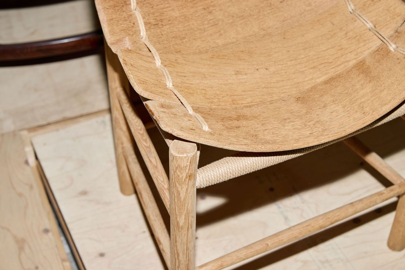 Close-up of a handmade wooden chair with a natural finish, featuring a woven seat and visible stitching along the edge. Close-up of a handmade wooden chair with a natural finish, featuring a woven seat and visible stitching along the edge.