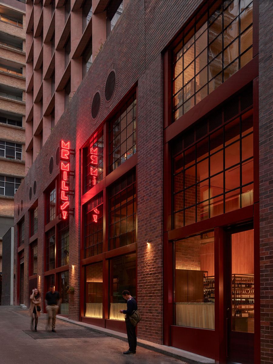 A stylish brick building with large windows and a neon sign reading "MrMills," featuring two pedestrians in a dimly lit urban alley. A stylish brick building with large windows and a neon sign reading "MrMills," featuring two pedestrians in a dimly lit urban alley.