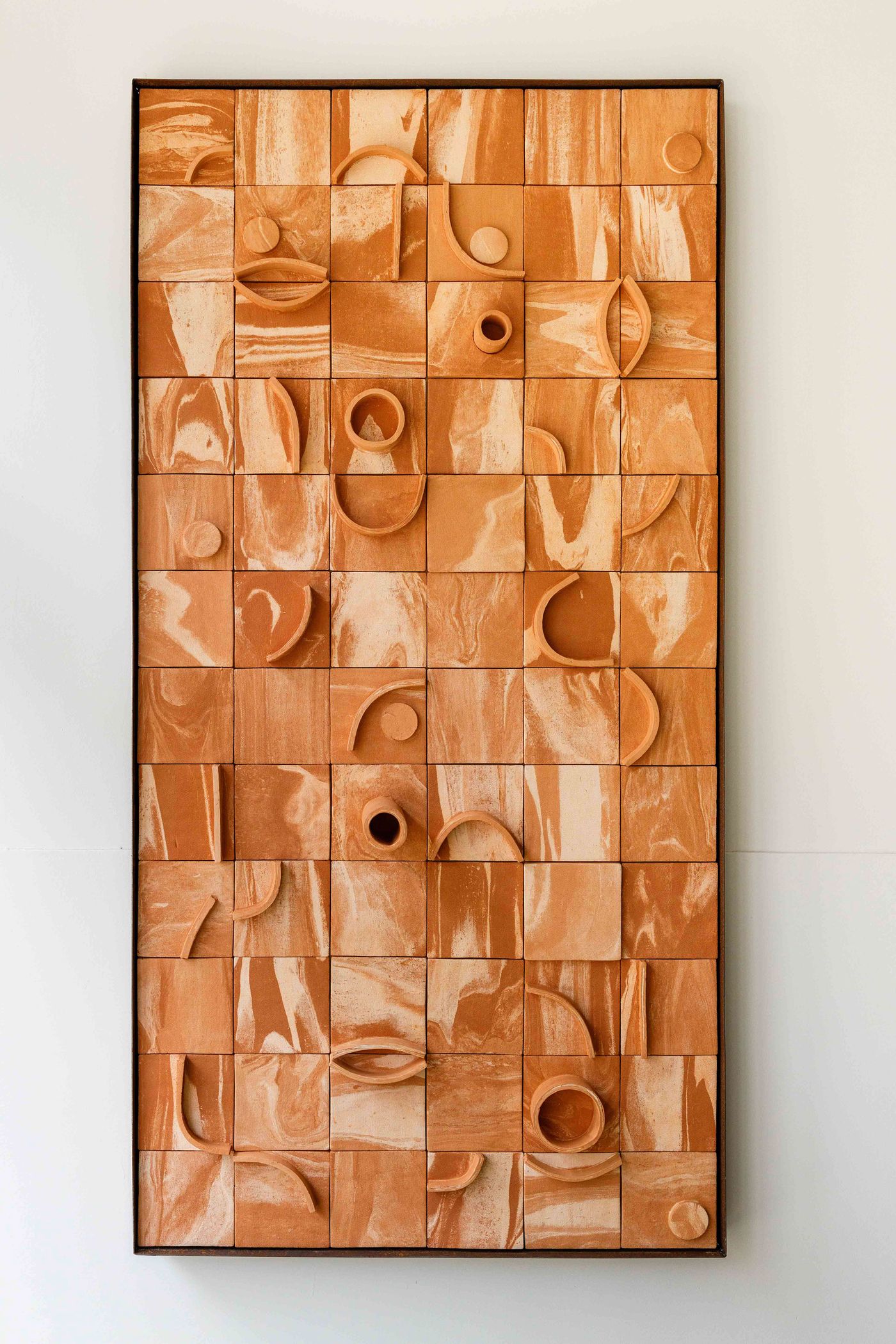 A large, rectangular wall art piece by Pareidolia Design, composed of an array of terracotta-colored ceramic tiles, each featuring unique organic shapes and abstract relief patterns. The tiles are arranged in a grid, showcasing various cut-outs, curves, and circular elements that create a dynamic, sculptural effect against a plain white wall.