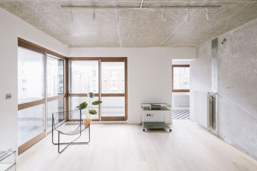 Bright, modern living space featuring large windows, a minimalist wire chair, and a small glass table with ornamental plants.