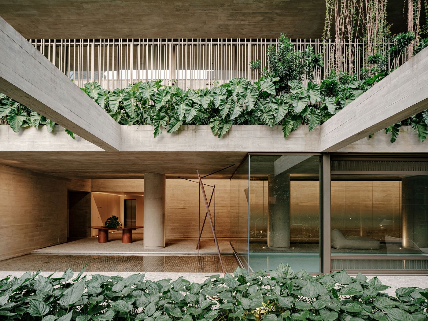 A captivating view of this project's integrated landscape and architecture, where broad concrete planes are softened by abundant tropical greenery overflowing from planters. A serene reflecting pool adds a tranquil element, while large glass panels offer glimpses into warm, inviting interior spaces, blurring the lines between indoor and outdoor. A captivating view of this project's integrated landscape and architecture, where broad concrete planes are softened by abundant tropical greenery overflowing from planters. A serene reflecting pool adds a tranquil element, while large glass panels offer glimpses into warm, inviting interior spaces, blurring the lines between indoor and outdoor.