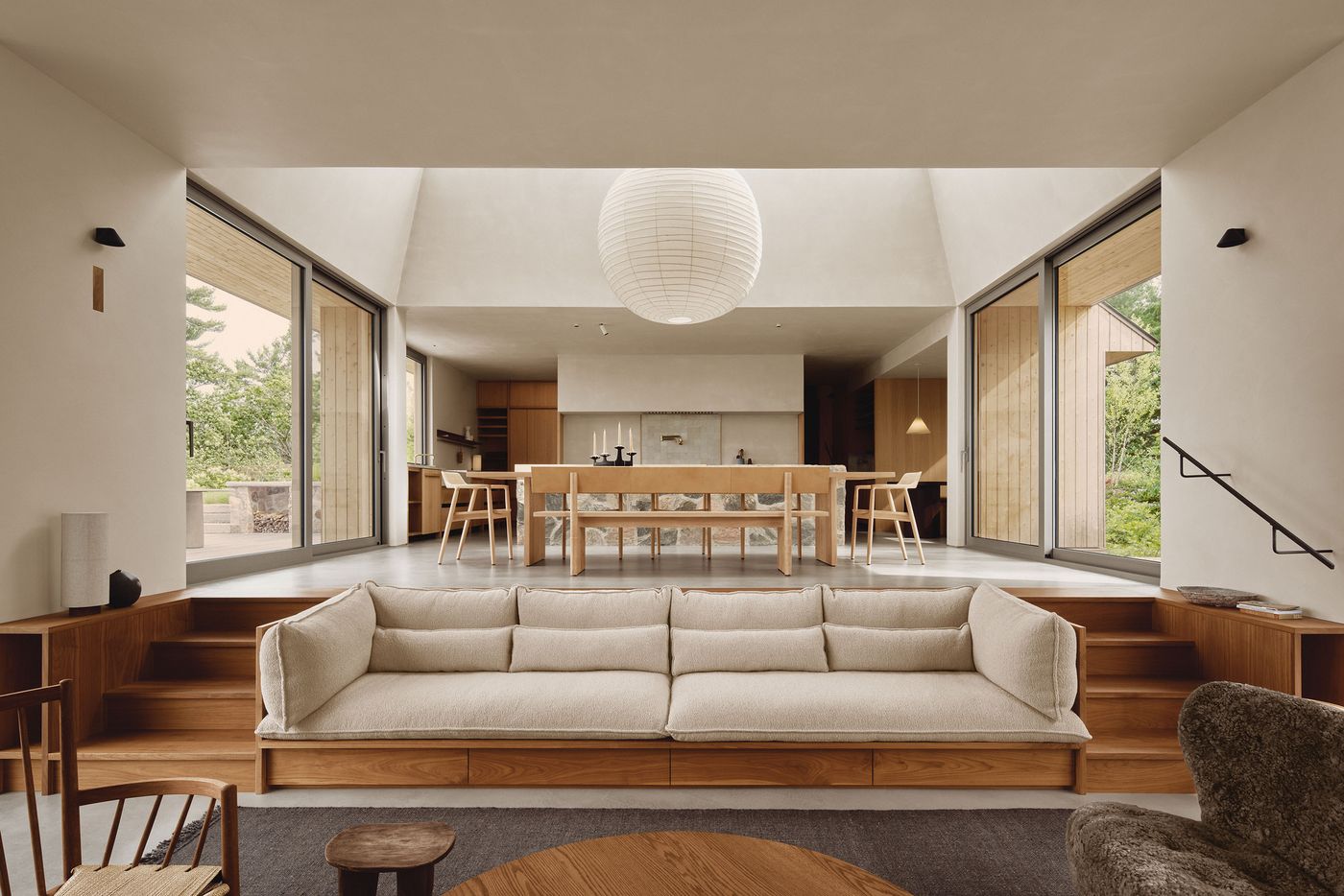 Modern living area with a cream couch, wooden dining set, and large windows overlooking a garden, styled in minimalist decor. Modern living area with a cream couch, wooden dining set, and large windows overlooking a garden, styled in minimalist decor.