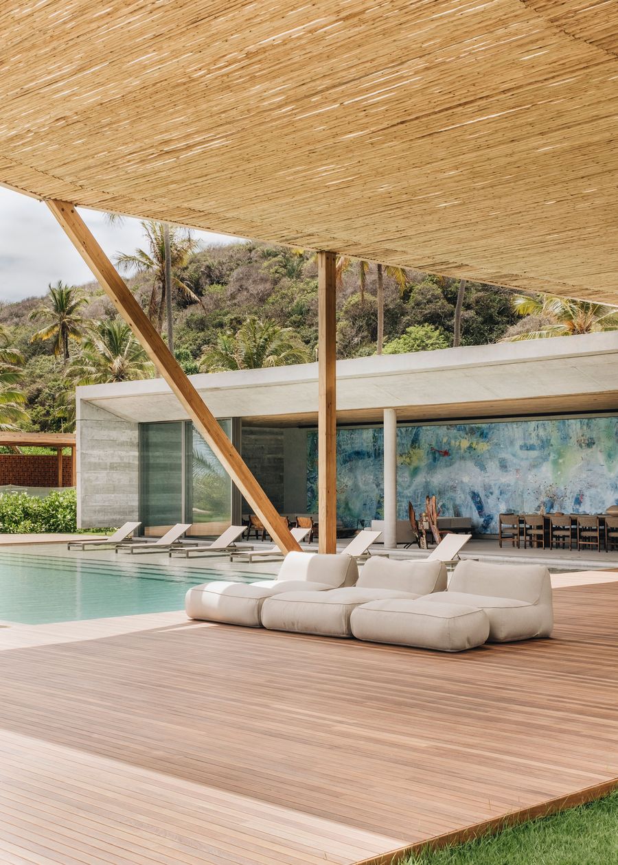 A modern outdoor lounge area features plush seating near a serene pool, surrounded by tropical greenery and a vibrant mural backdrop.