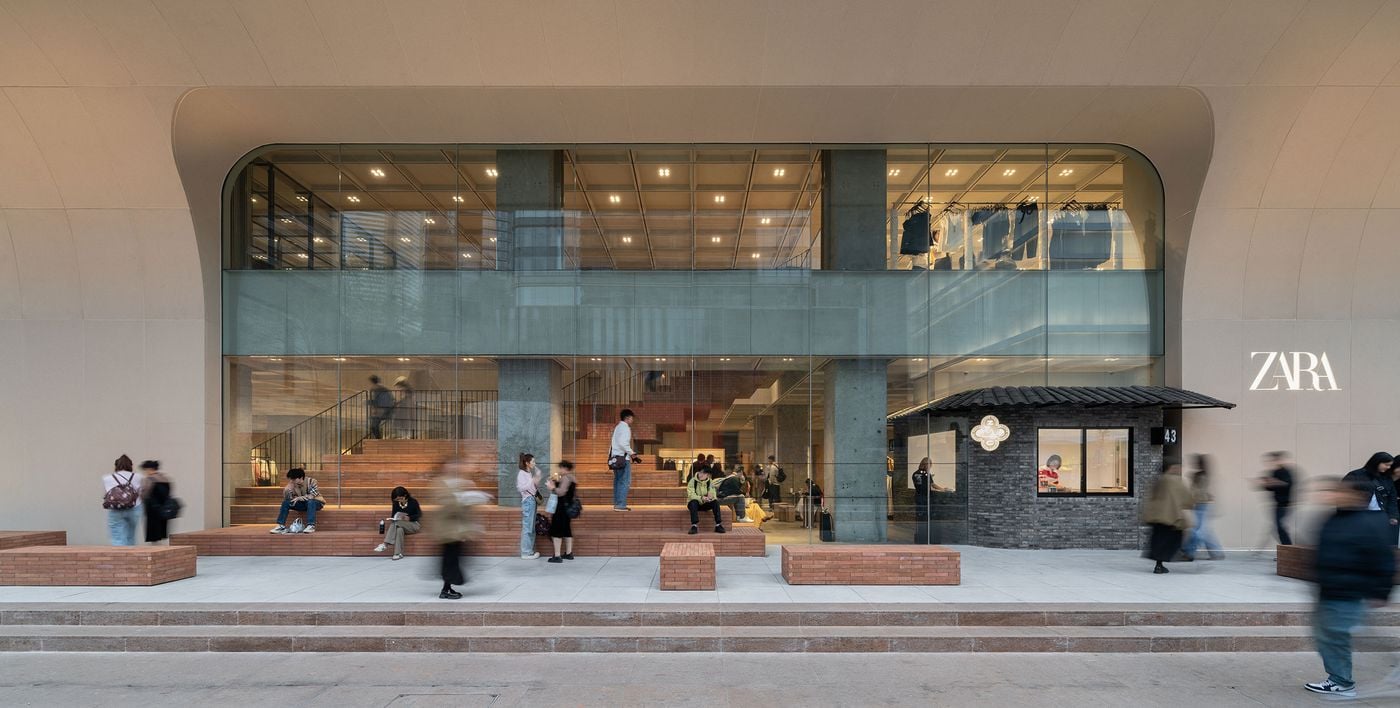 Zara storefront with modern architecture; shoppers and visitors interact outside, featuring brick seating and a quaint kiosk. Zara storefront with modern architecture; shoppers and visitors interact outside, featuring brick seating and a quaint kiosk.