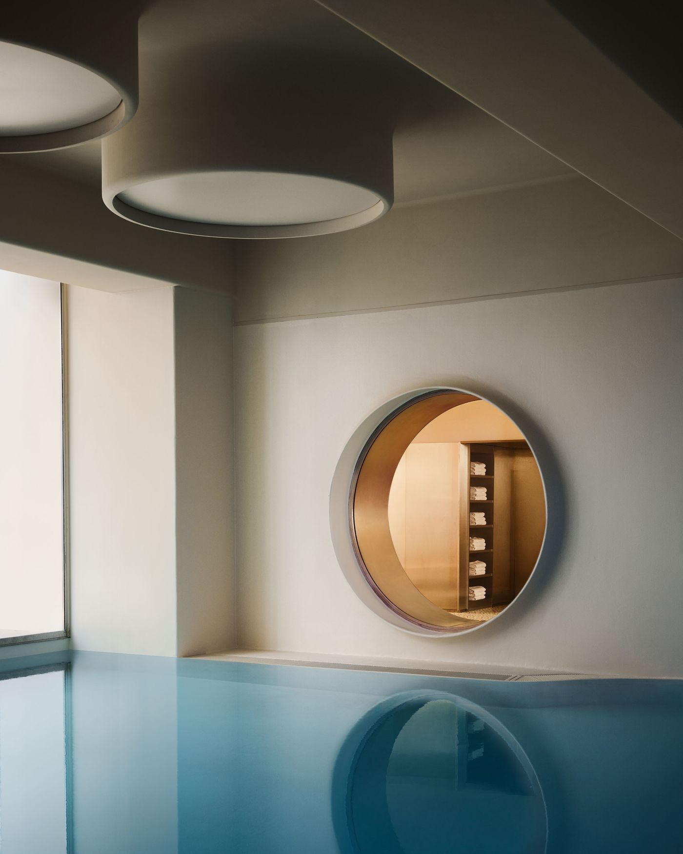 The renovated Ken Club pool pairs calm blue water with pale walls, circular ceiling lights and a metal-lined porthole connecting to an adjoining room. Reflections on the water double the rounded forms, giving the space an almost cinematic serenity within the club’s otherwise more exuberant interiors. The renovated Ken Club pool pairs calm blue water with pale walls, circular ceiling lights and a metal-lined porthole connecting to an adjoining room. Reflections on the water double the rounded forms, giving the space an almost cinematic serenity within the club’s otherwise more exuberant interiors.