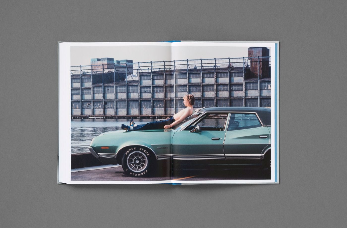 A sandy-haired young man reclines bare-chested on the bonnet of a sea-green Ford Gran Torino, legs stretched out in dark jeans, gazing across the water. Behind him a derelict waterfront warehouse with a grid of broken windows sets a scene of languid urban leisure in this colour spread from Don't Worry Boys. A sandy-haired young man reclines bare-chested on the bonnet of a sea-green Ford Gran Torino, legs stretched out in dark jeans, gazing across the water. Behind him a derelict waterfront warehouse with a grid of broken windows sets a scene of languid urban leisure in this colour spread from Don't Worry Boys.