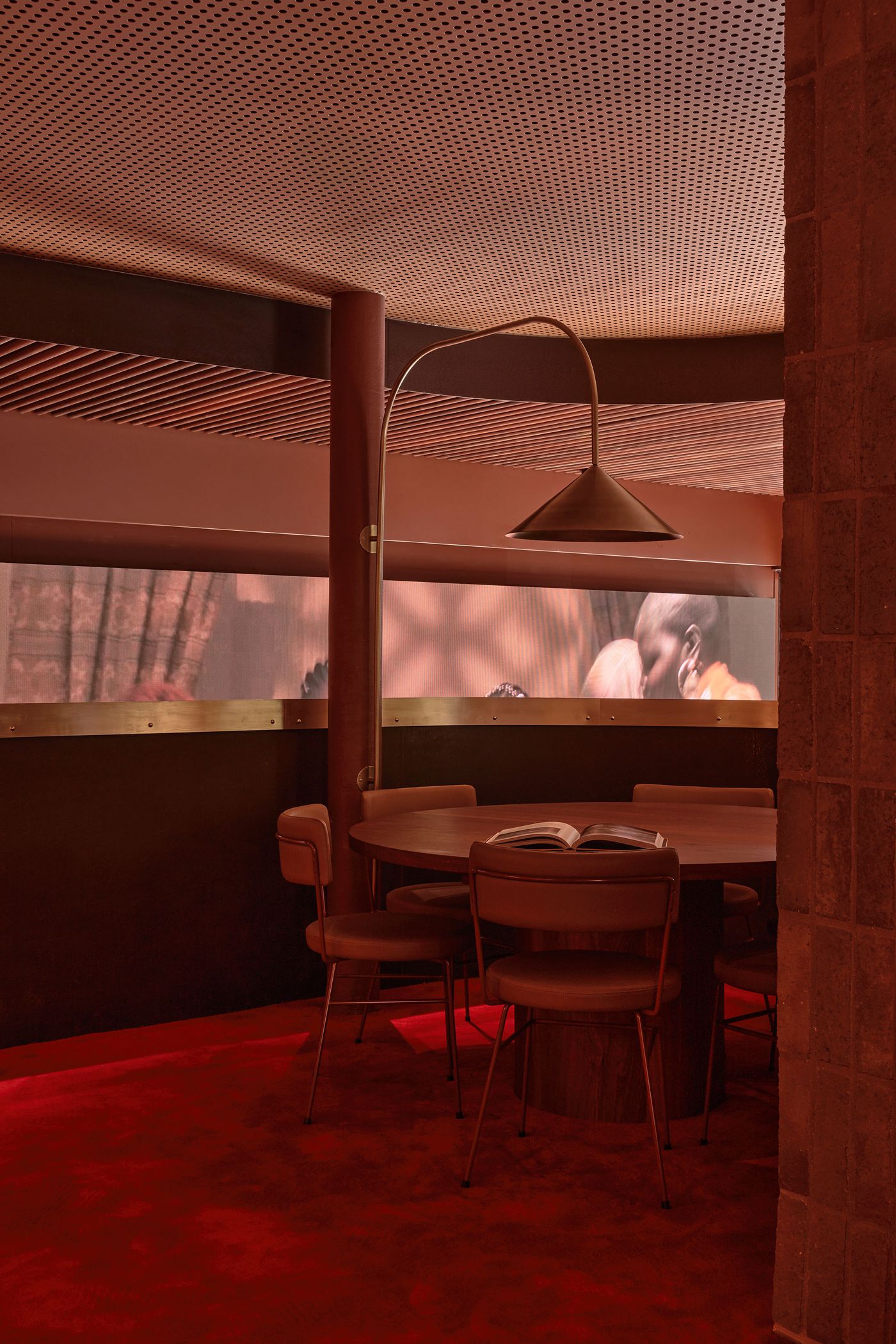 Modern, inviting interior featuring a round table with chairs and warm lighting, set against a backdrop of muted red tones. Modern, inviting interior featuring a round table with chairs and warm lighting, set against a backdrop of muted red tones.