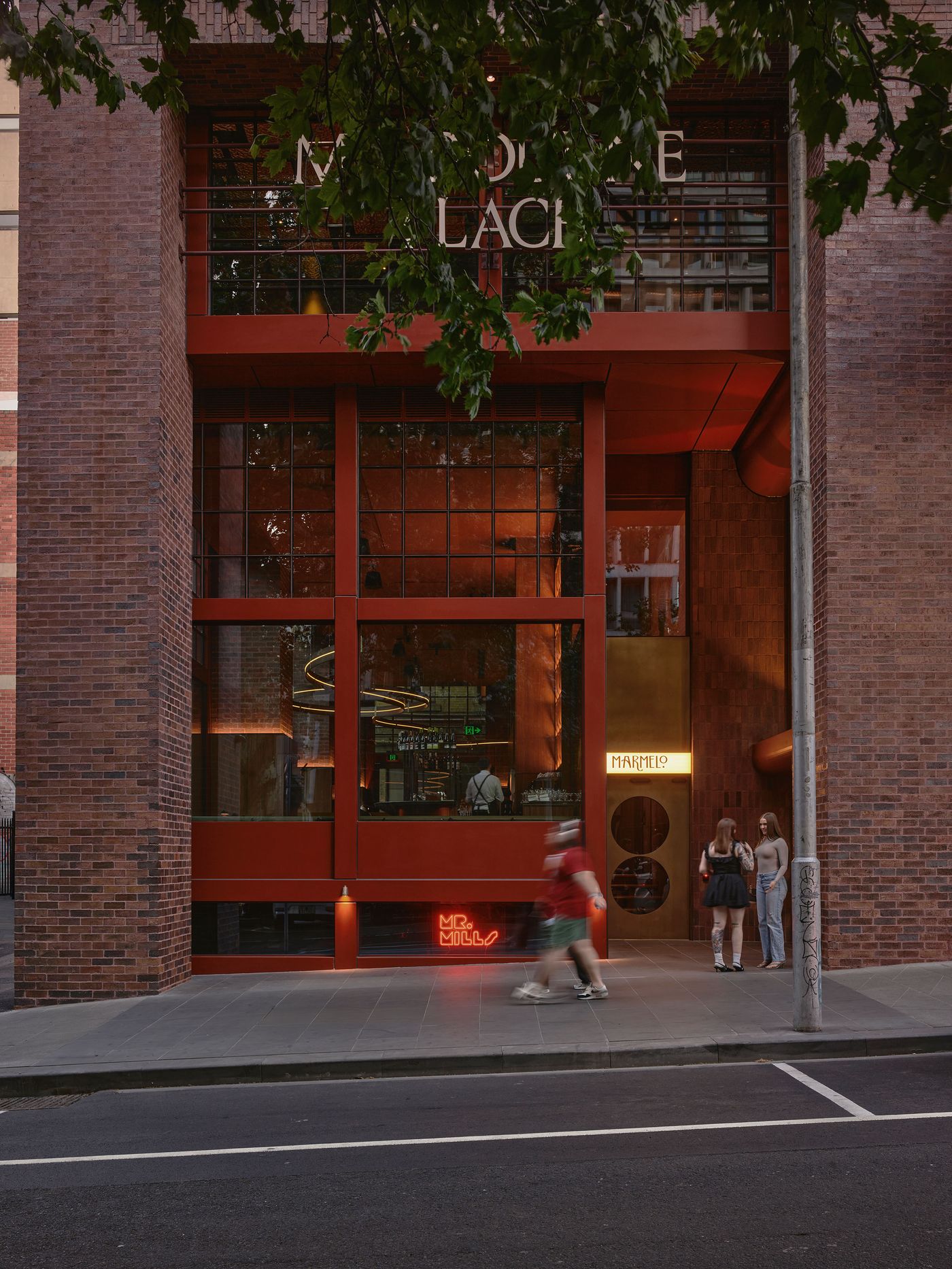 Urban scene featuring a modern restaurant entrance with large windows, neon signs, and people walking by in the evening light. Urban scene featuring a modern restaurant entrance with large windows, neon signs, and people walking by in the evening light.
