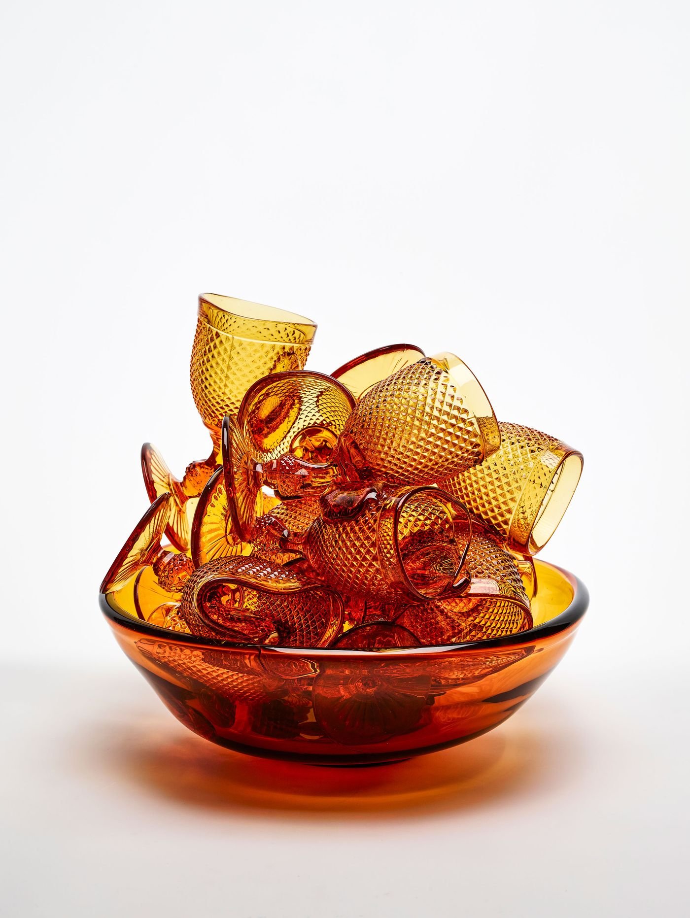 A captivating sculptural glass object features numerous amber-hued, diamond-patterned goblets, seemingly overflowing from a matching translucent amber bowl. Hand-crafted by Vista Alegre, it creates a sense of abundant, warm opulence through its rich color and textured forms.