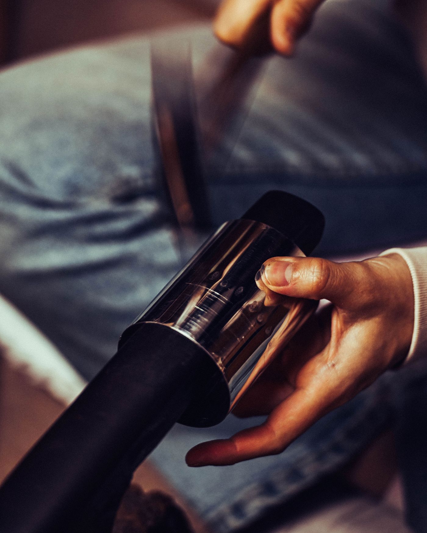 A close-up of a hand holding a shiny metal object, with a blurred background showcasing a person working on a project.