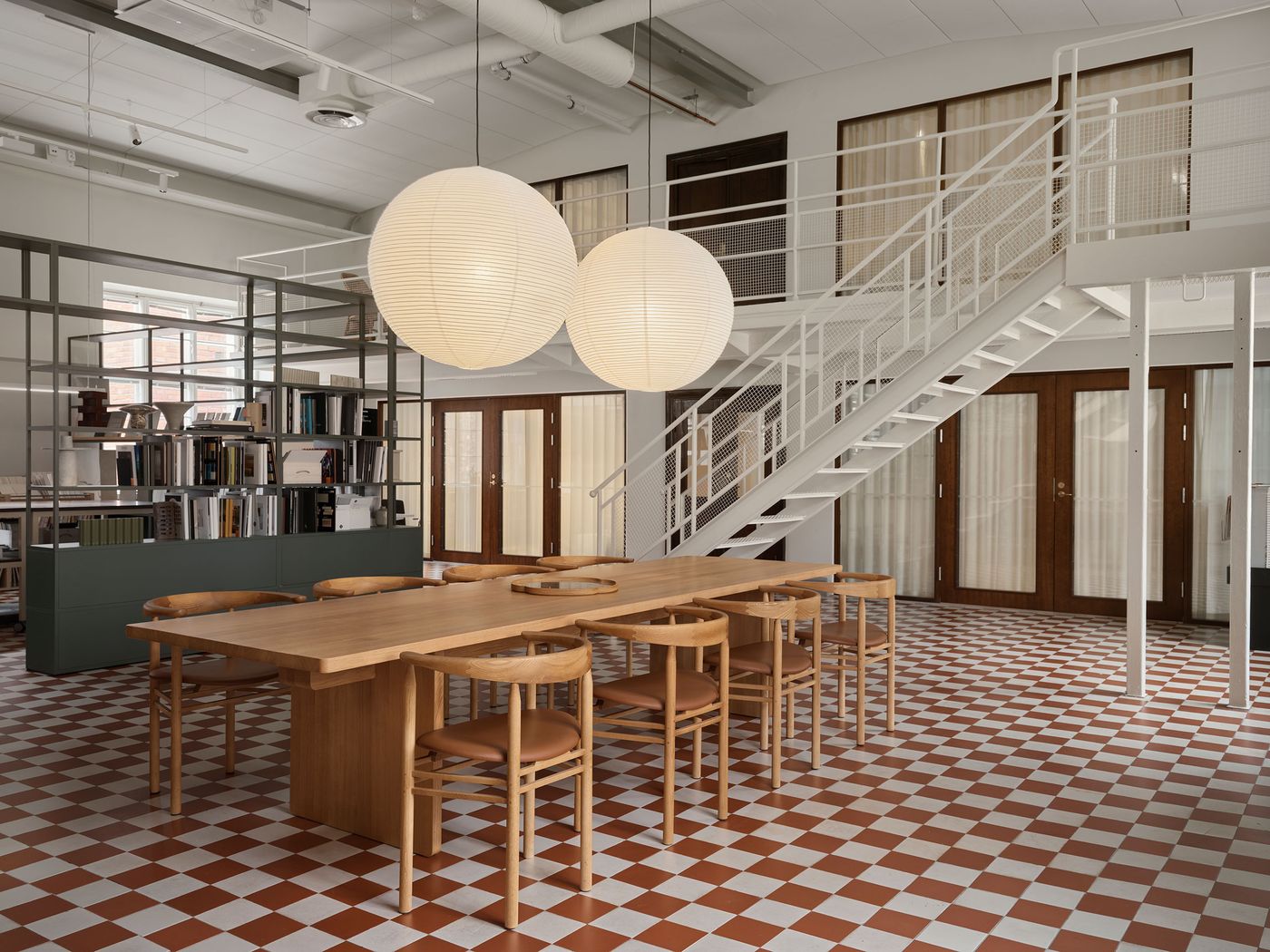 An expansive open-plan space features a modern dining setup with wooden furniture on a striking red and white checkerboard floor. A minimalist white metal staircase ascends to an upper level, seamlessly blending industrial elements with Scandinavian design aesthetics. An expansive open-plan space features a modern dining setup with wooden furniture on a striking red and white checkerboard floor. A minimalist white metal staircase ascends to an upper level, seamlessly blending industrial elements with Scandinavian design aesthetics.